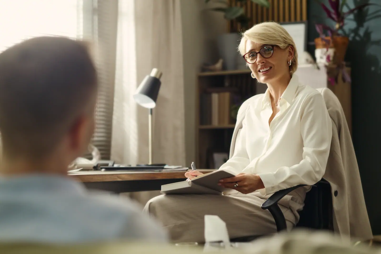Counselor with blonde hair taking notes during a conversation