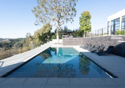 A pool in the backyard of a modern home, surrounded by lush greenery, at Bliss Recovery LA